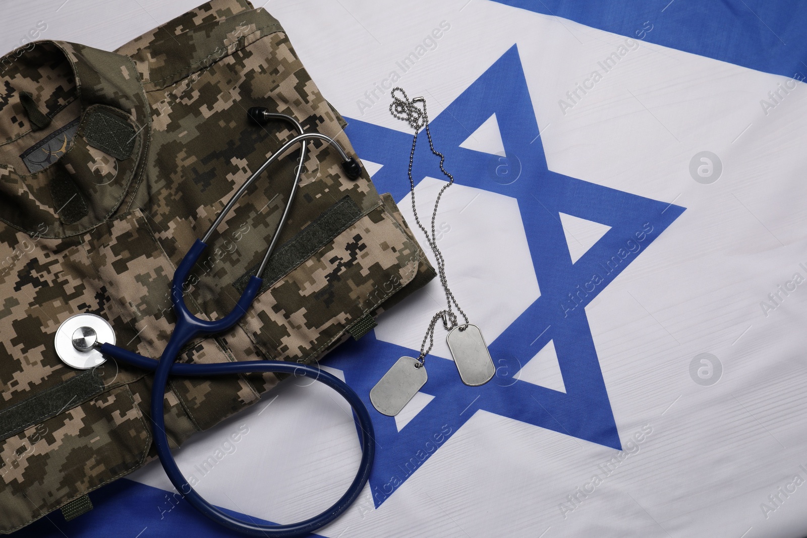 Photo of Stethoscope, tags and military uniform on flag of Israel, flat lay