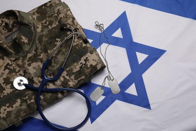 Stethoscope, tags and military uniform on flag of Israel, flat lay