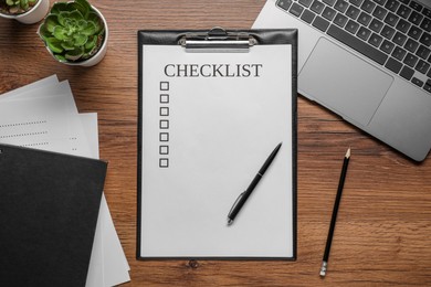 Photo of Clipboard with checklist, pen and laptop on wooden table, flat lay