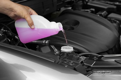 Photo of Man pouring liquid from plastic canister into car washer fluid reservoir, closeup