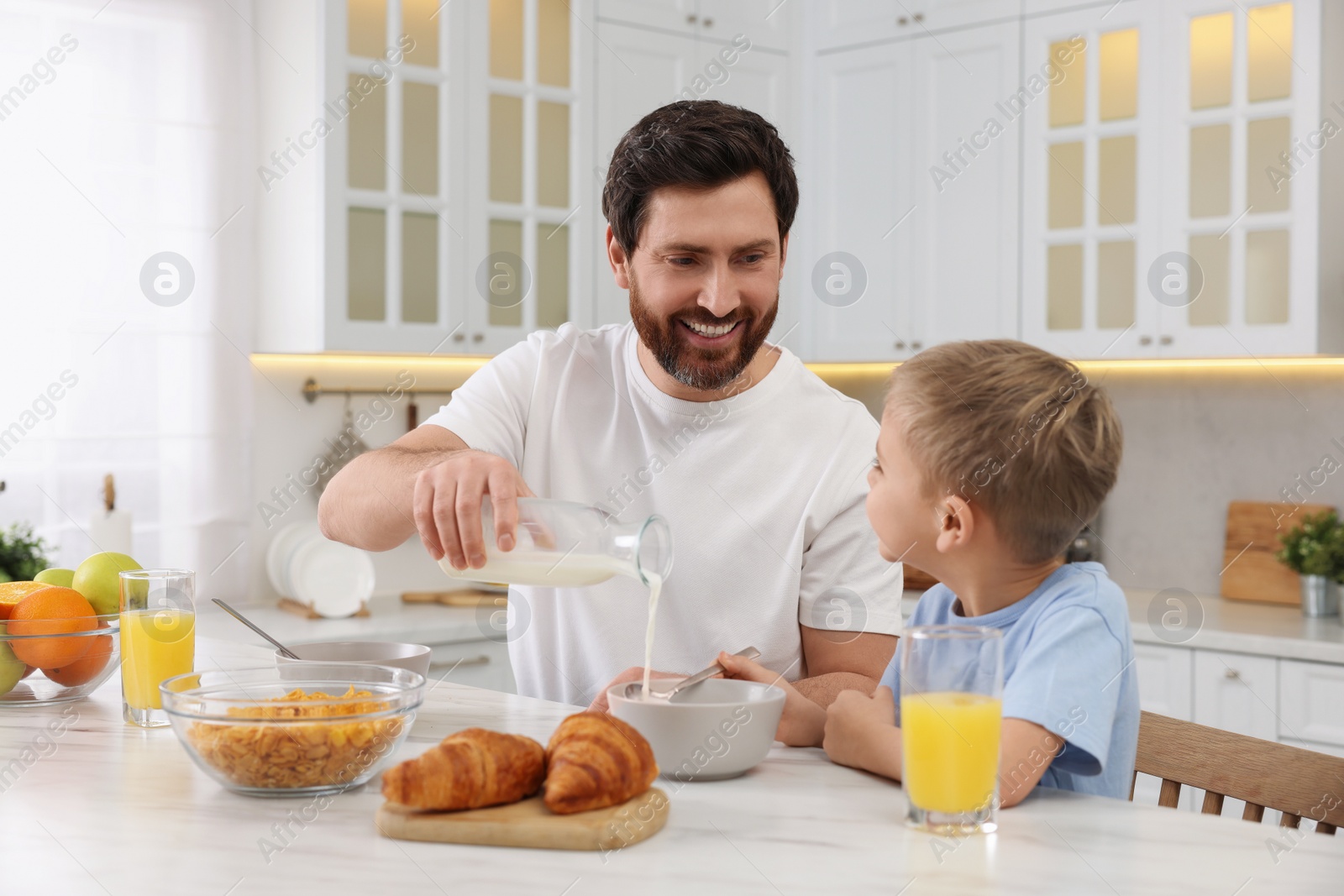 Photo of Father and his cute little son having breakfast at table in kitchen