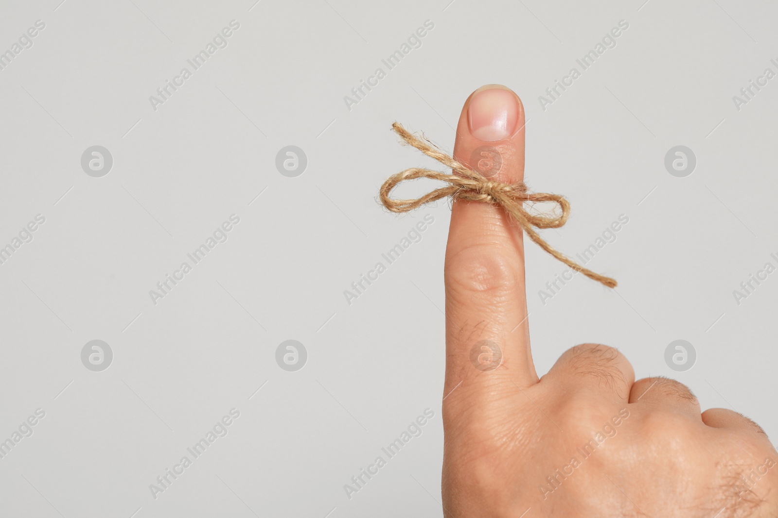 Photo of Man showing index finger with tied bow as reminder on light grey background, closeup. Space for text