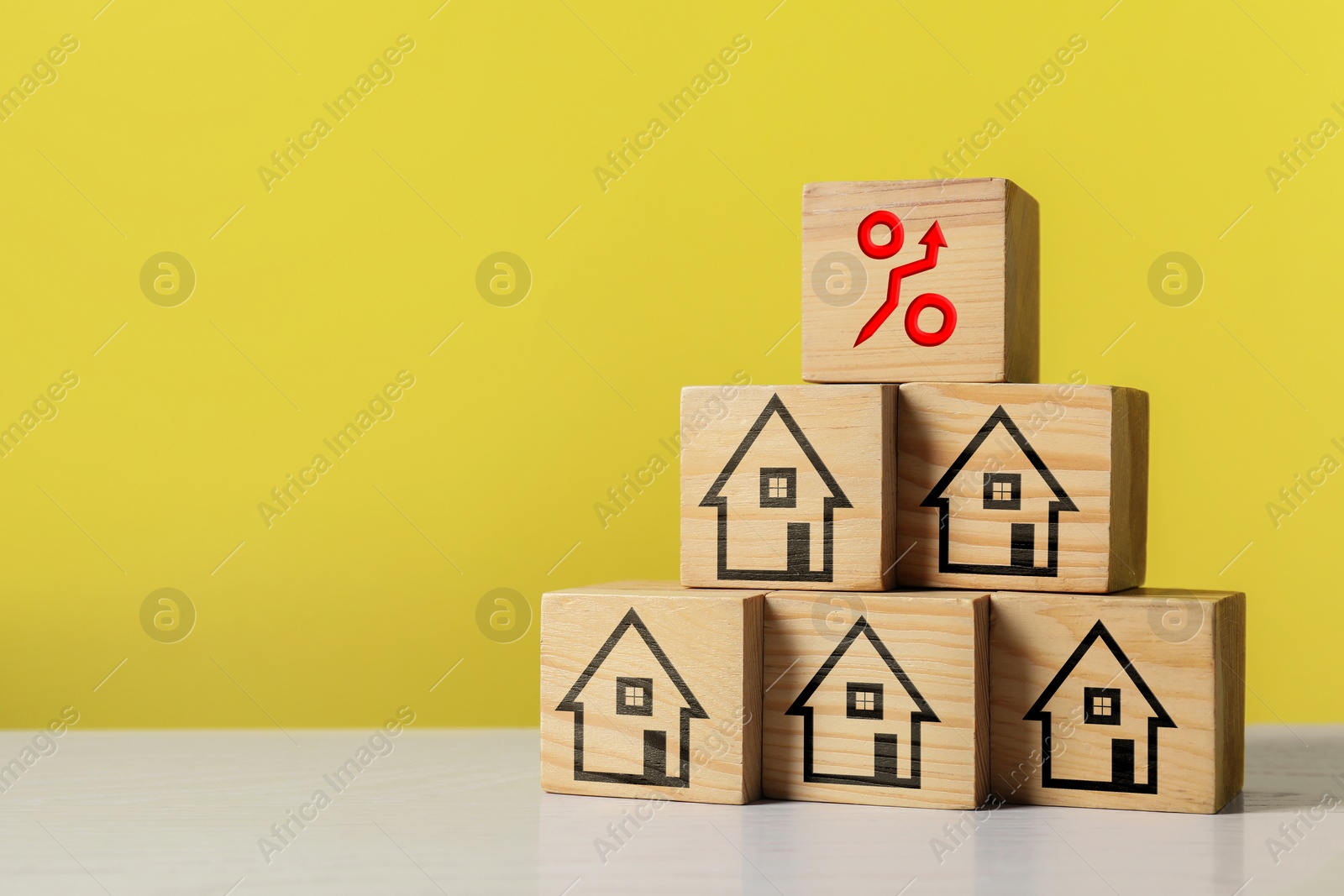 Image of Mortgage rate rising illustrated by percent sign with upward arrow. Pyramid of wooden cubes with house icons on table, space for text