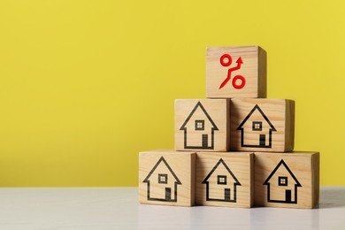 Image of Mortgage rate rising illustrated by percent sign with upward arrow. Pyramid of wooden cubes with house icons on table, space for text