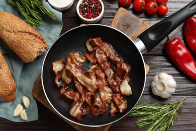 Delicious bacon slices in frying pan and products on wooden table, flat lay