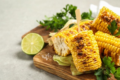 Photo of Tasty grilled corn cobs with parsley on grey table, closeup. Space for text