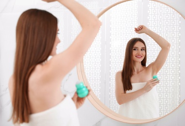 Photo of Beautiful young woman applying deodorant after shower in bathroom