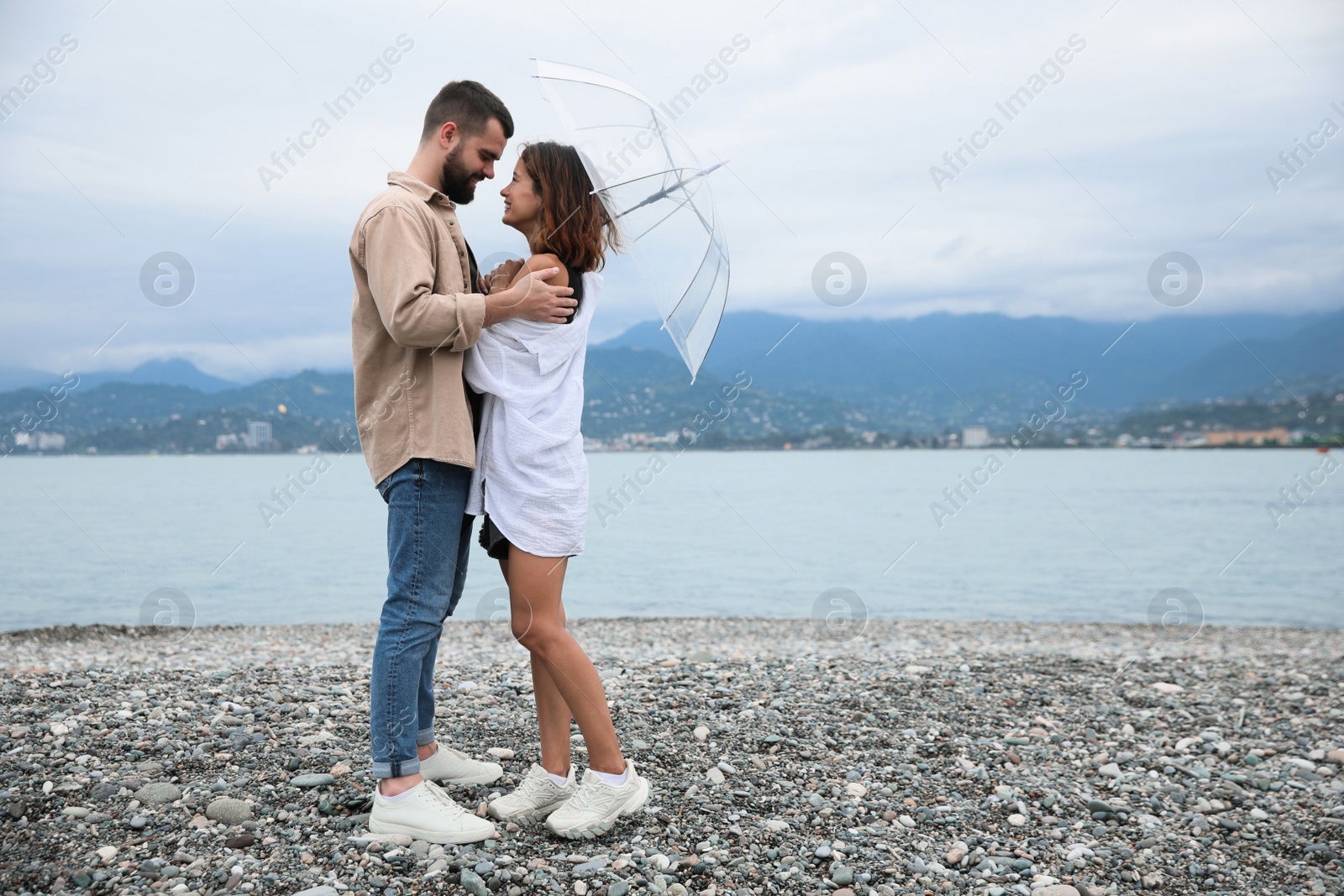 Photo of Young couple with umbrella enjoying time together under rain on beach, space for text