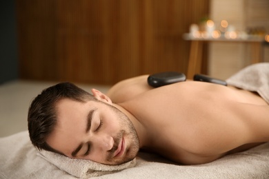 Handsome man receiving hot stone massage in spa salon. Space for text