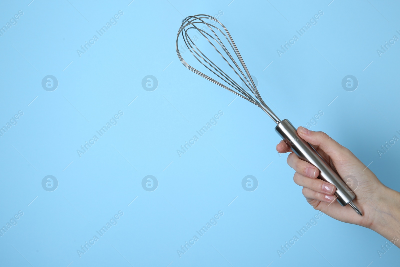 Photo of Woman holding metal whisk on light blue background, closeup. Space for text