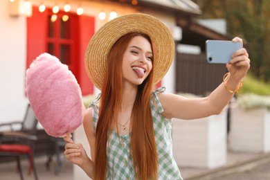 Photo of Funny woman with cotton candy taking selfie outdoors