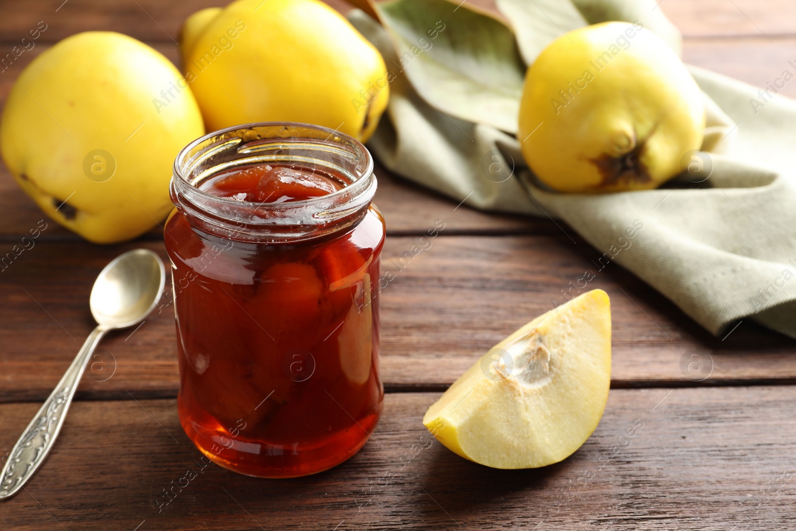 Photo of Tasty homemade quince jam in jar and fruits on wooden table