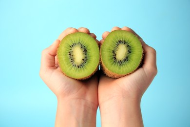 Woman holding delicious fresh kiwi on light blue background, closeup