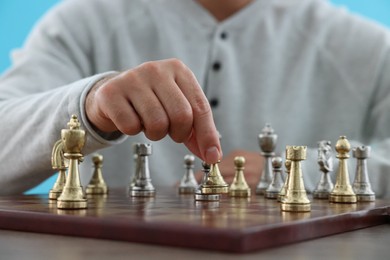 Man moving chess piece on checkerboard against light blue background, closeup