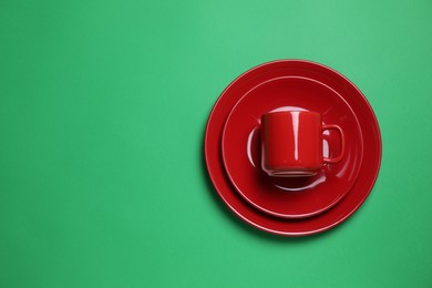 Set of red ceramic dishware on green background, top view. Space for text