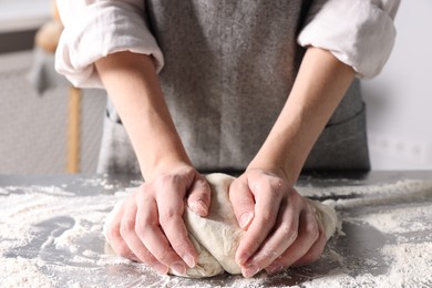 Photo of Woman kneading dough at table in kitchen, closeup