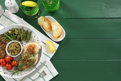 Tasty chicken, vegetables, drink with tarragon and pesto sauce served on green wooden table, flat lay. Space for text