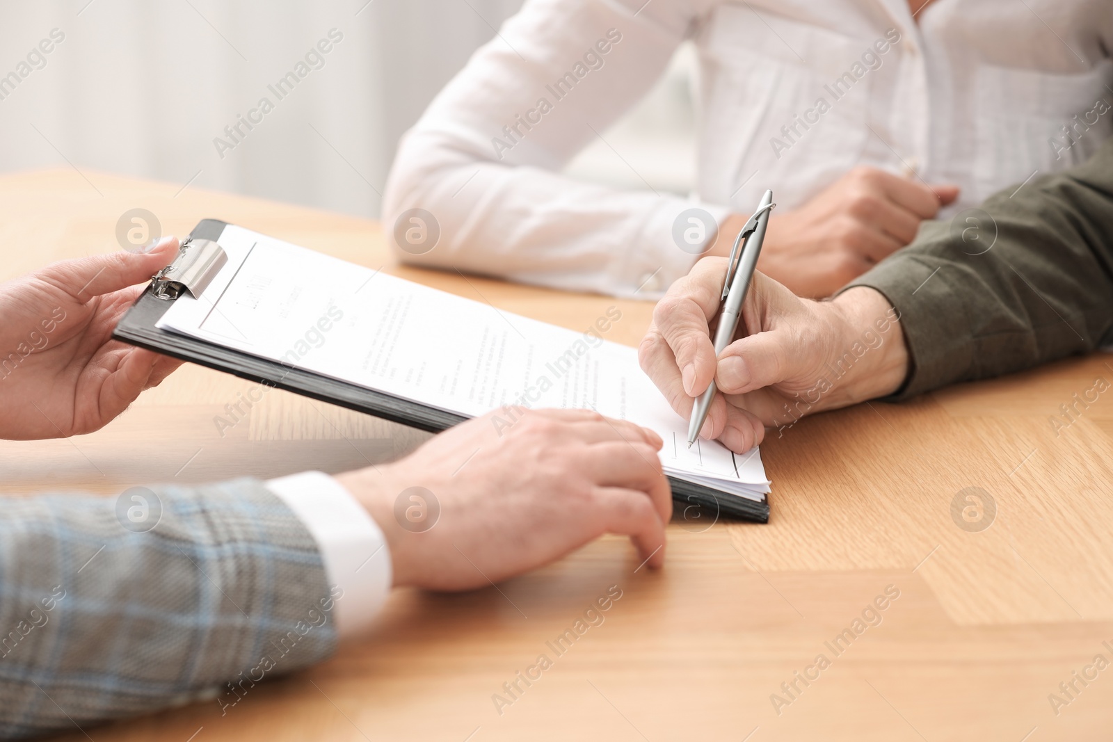 Photo of Notary showing senior couple where to sign Last Will and Testament at wooden table indoors, closeup