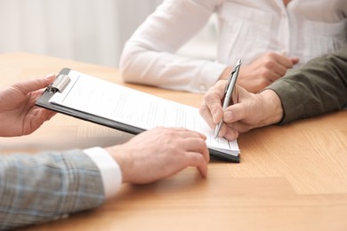 Notary showing senior couple where to sign Last Will and Testament at wooden table indoors, closeup