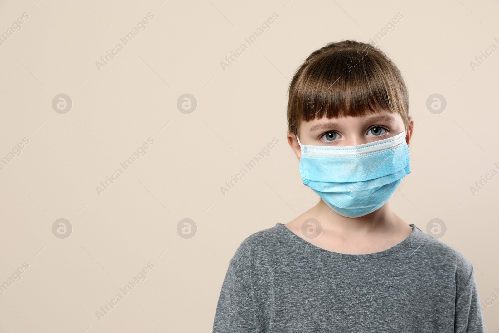 Photo of Little girl in medical mask on beige background, space for text. Virus protection