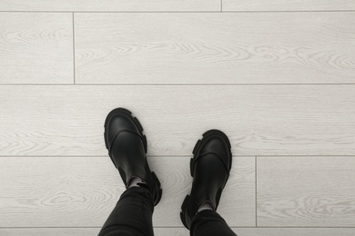 Person in black boots standing on wooden floor, top view. Space for text