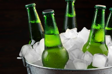 Photo of Metal bucket with bottles of beer and ice cubes on dark background, closeup