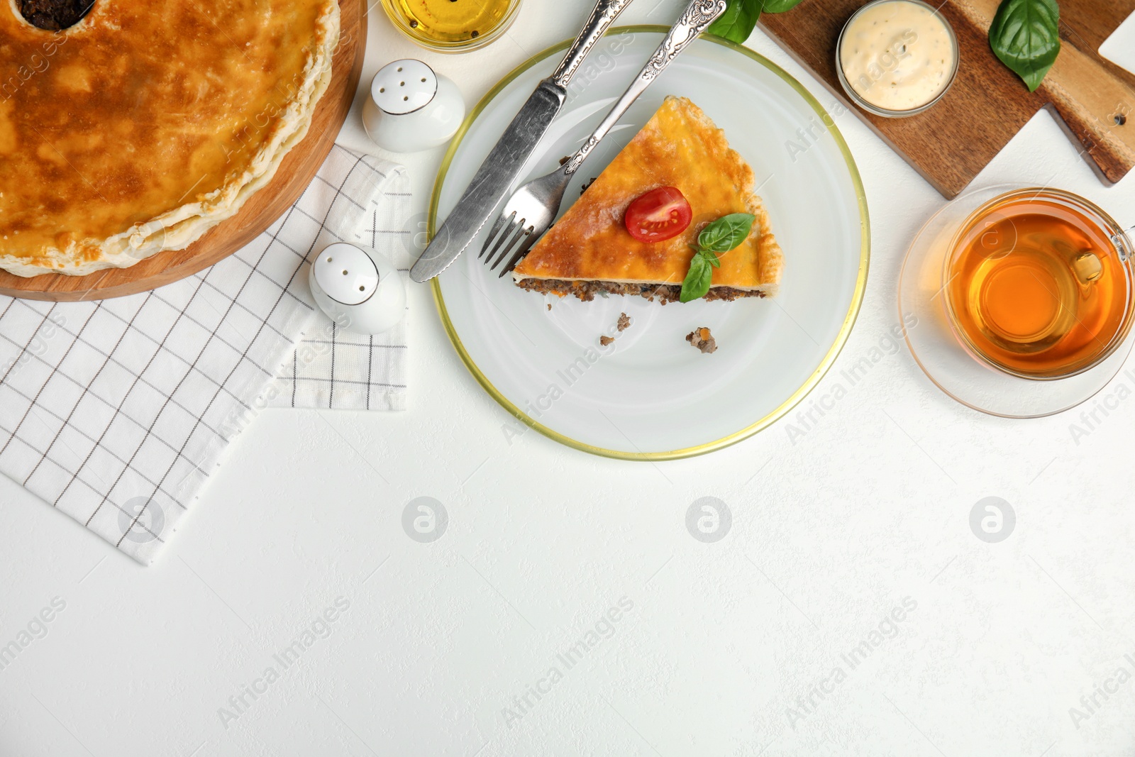 Photo of Delicious pie with minced meat, tomato and tea served on white table, flat lay. Space for text