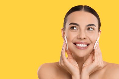 Beautiful woman removing makeup with cotton pads on yellow background. Space for text