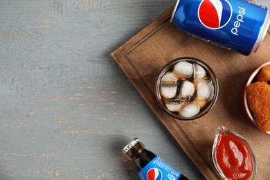 Photo of MYKOLAIV, UKRAINE - FEBRUARY 15, 2021: Different Pepsi drinks and snack on grey wooden table, flat lay. Space for text