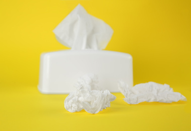 Photo of Used paper tissues and white holder on yellow background, closeup