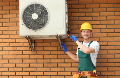 Photo of Professional technician repairing modern air conditioner outdoors