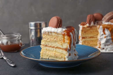 Photo of Piece of delicious homemade cake with caramel sauce and macaron on table