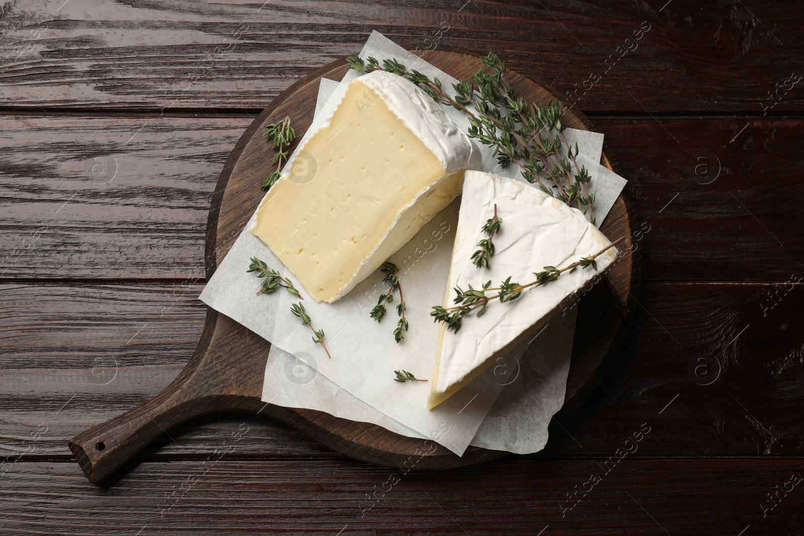 Photo of Board with pieces of tasty camembert cheese and thyme on wooden table, top view