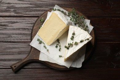 Board with pieces of tasty camembert cheese and thyme on wooden table, top view