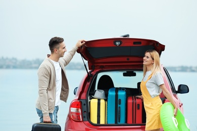 Couple packing suitcases in car trunk on riverside