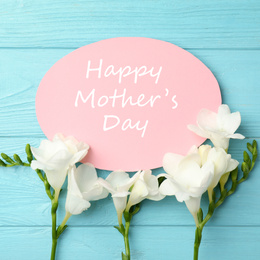 Image of Card with phrase HAPPY MOTHER'S DAY and beautiful flowers on light blue wooden background, flat lay