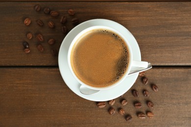 Cup of tasty coffee and beans on wooden table, flat lay