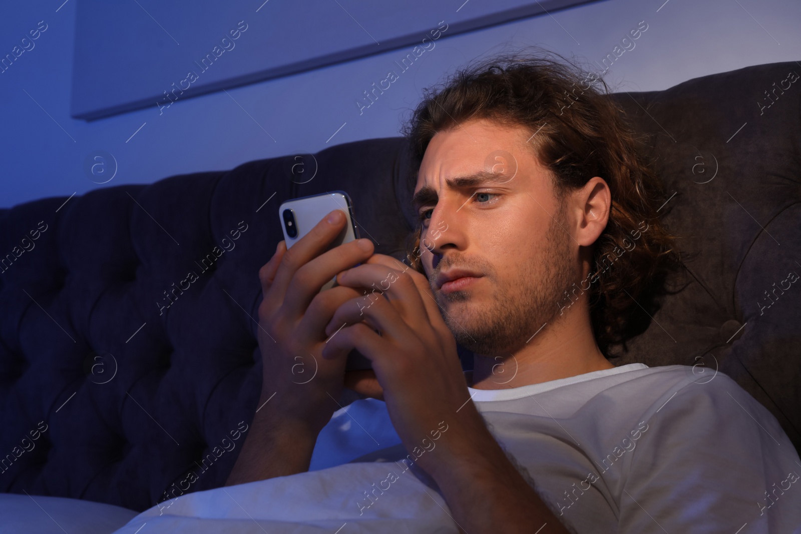 Photo of Handsome young man using smartphone in dark room at night. Bedtime