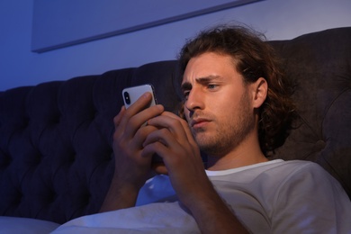 Photo of Handsome young man using smartphone in dark room at night. Bedtime