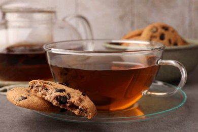 Photo of Cup of hot tea and chocolate chip cookies on grey table, closeup