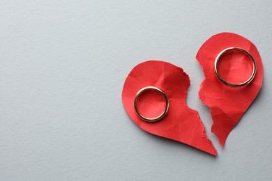 Photo of Broken heart. Halves of torn red paper heart and wedding rings on white background, top view. Space for text
