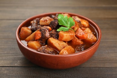 Photo of Delicious beef stew with carrots, parsley and potatoes on wooden table, closeup