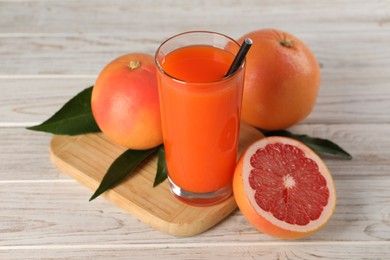 Photo of Tasty grapefruit juice in glass and fresh fruits on light wooden table