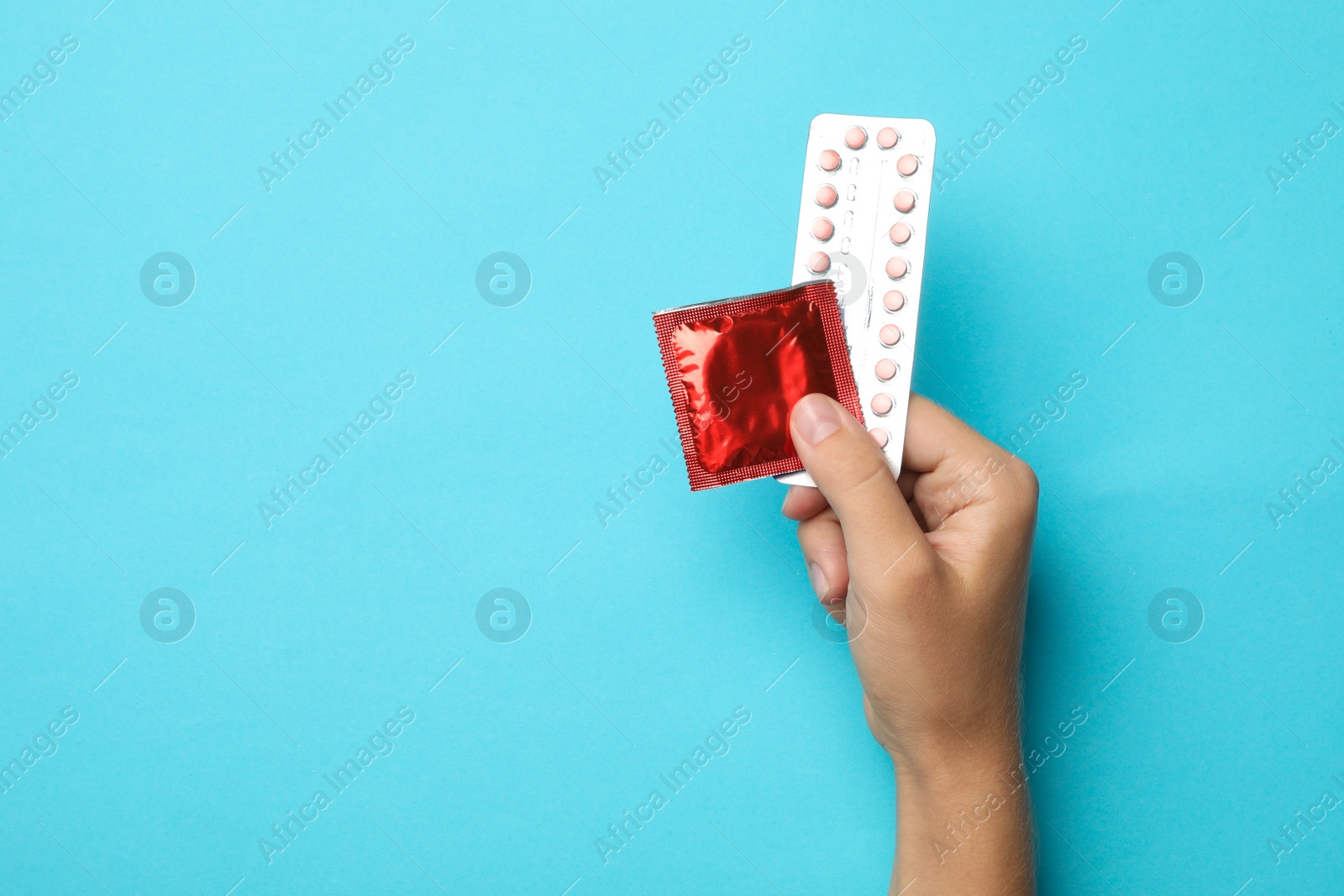 Photo of Woman holding condom and birth control pills on blue background, top view with space for text. Safe sex