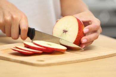 Photo of Woman cutting fresh apple at wooden table indoors, closeup