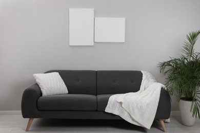 Photo of Blank canvas on wall over comfortable sofa indoors. Space for design