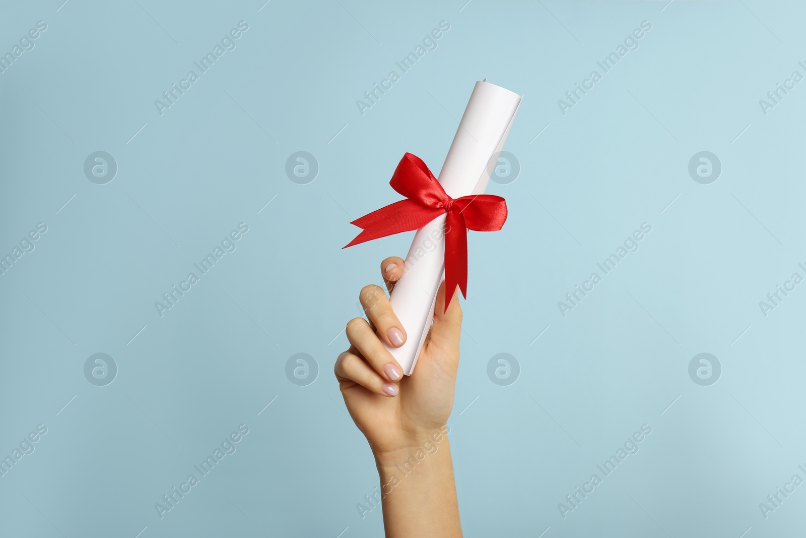 Photo of Student holding rolled diploma with red ribbon on light blue background, closeup