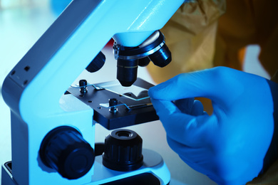 Photo of Scientist in chemical protective suit using microscope at table, closeup. Virus research