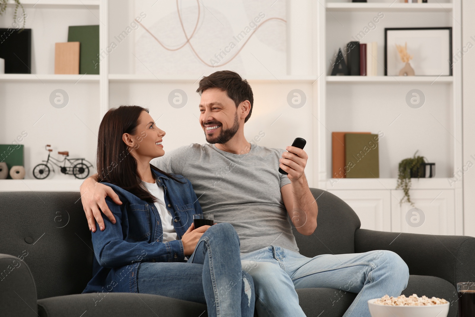 Photo of Happy couple spending time together at home. Man changing TV channels with remote control