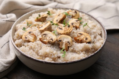 Photo of Delicious barley porridge with mushrooms and microgreens in bowl on table, closeup